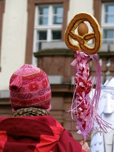 A child participating in Heidelberg's Sommertagszug festival, which celebrates spring's arrival, holds a pretzel and egg decoration on a stick.