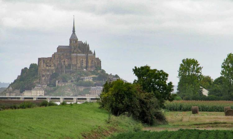 Mont-Saint-Michel, surrounded by a green field on a grey day.