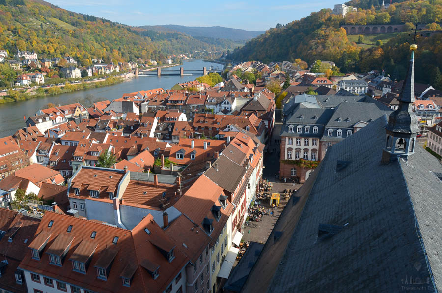 Looking east toward above the Neckar River, Staustufe Heidelberg (left), and the arches of the Heidelberg Castle grounds (right). The sky is blue and the hillsides' trees are covered in autumn colors.