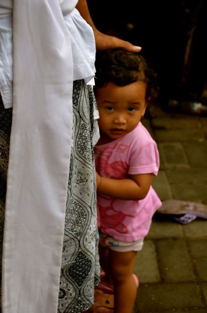 Balinese child peeking behind parent