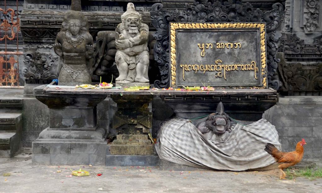 A chicken walks past a Balinese temple's statues, in Jimbaran.