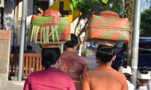 Women balance spiritual offering baskets on their heads in Ubud, Bali.