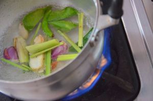 Lemongrass, shallots, and Kaffir lime leaves cook in boiling water on a gas stovetop in a cooking class kitchen in Bangkok, Thailand.