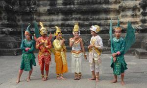 Six adults, dressed in traditional Cambodian costumes, stand near Angkor Wat.