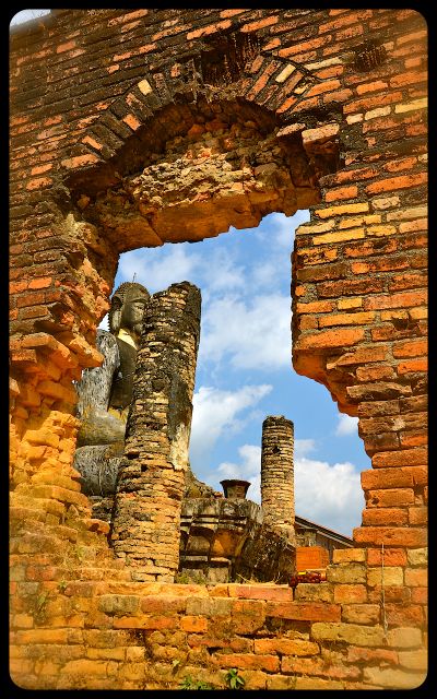 A glimpse of the damaged Buddha statue at Wat Pia Wat in Laos. The photo is taken through a broken-out hole in the brick wall.