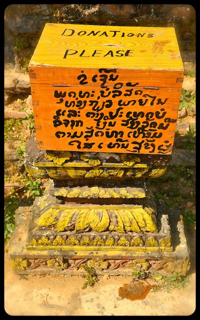 A donation box at the damaged Wat Phia Wat Temple in Laos. The writing on the box is English and Laotian. The English says, "Donations Please."