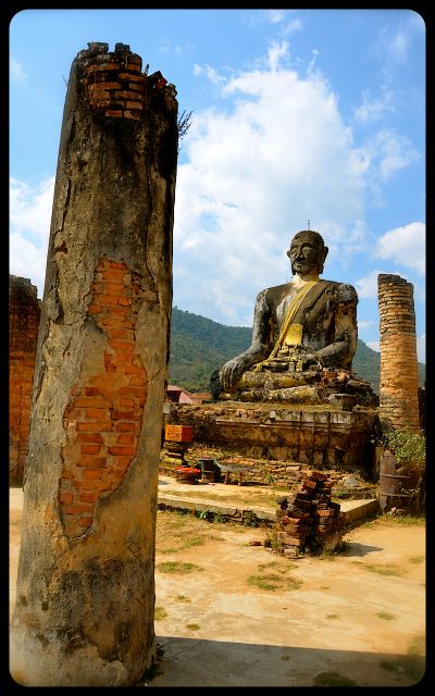 A ruined column and the damaged Buddha statue at Wat Phia Wat in Laos.