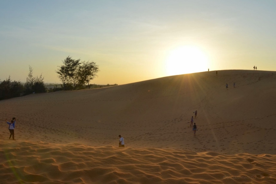 People walk across Mui Ne's sand dunes at sunset.