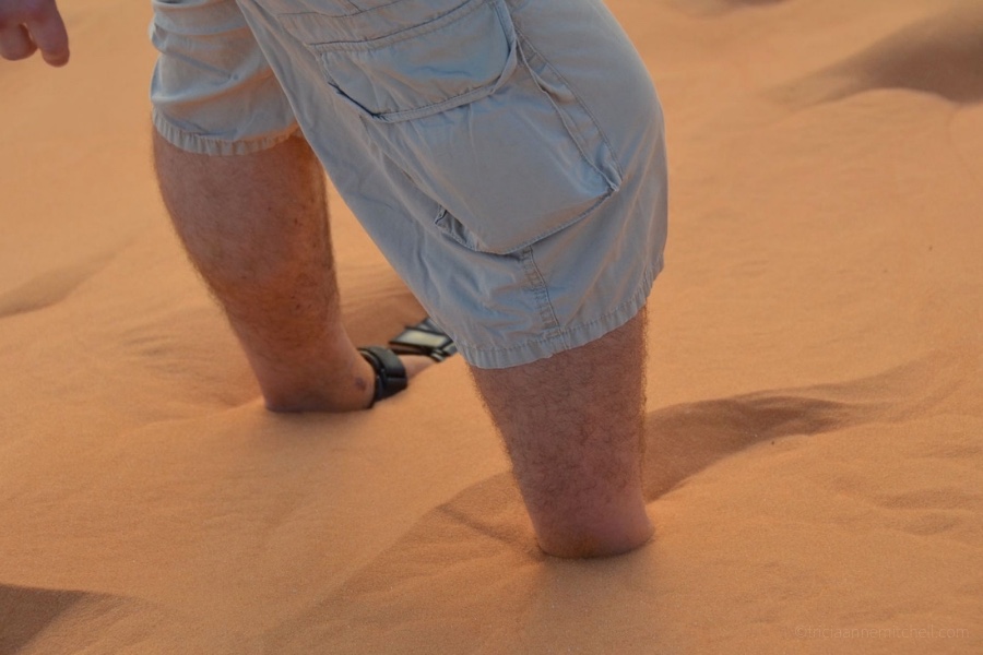 A man's legs are submerged in sand at the Mui Ne Red Sand Dunes in Vietnam.
