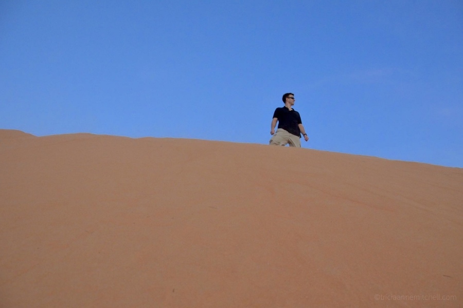A man stands atop the Mui Ne Sand Dune in Vietnam with a blue sky overhead.