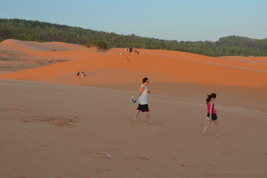 A couple walks across the Mui Ne Sand Dunes at sunset.