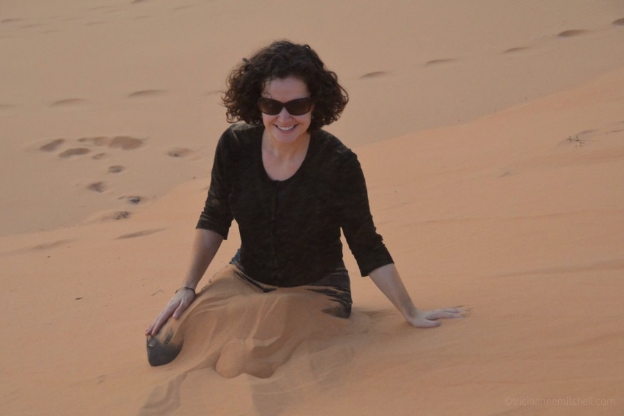 A woman sits on the Mui Ne Sand Dunes. Her legs are submerged in sand.