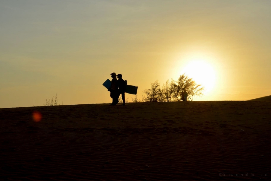 A pair of people holds plastic sandboards at Mui Ne, Vietnam's Red Sand Dunes.