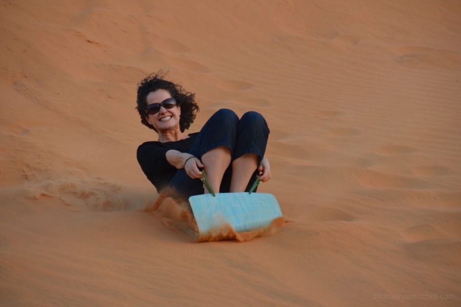 A woman slides down Mui Ne's Sand Dunes in Vietnam.