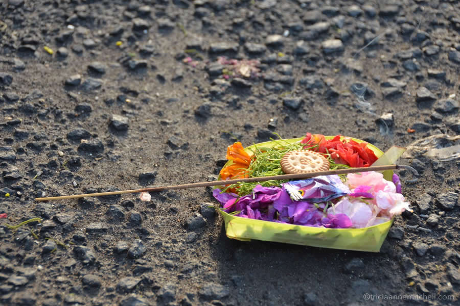 A Balinese spiritual offering (flowers, incense and a cookie) sits on the pavement in Jimbaran.
