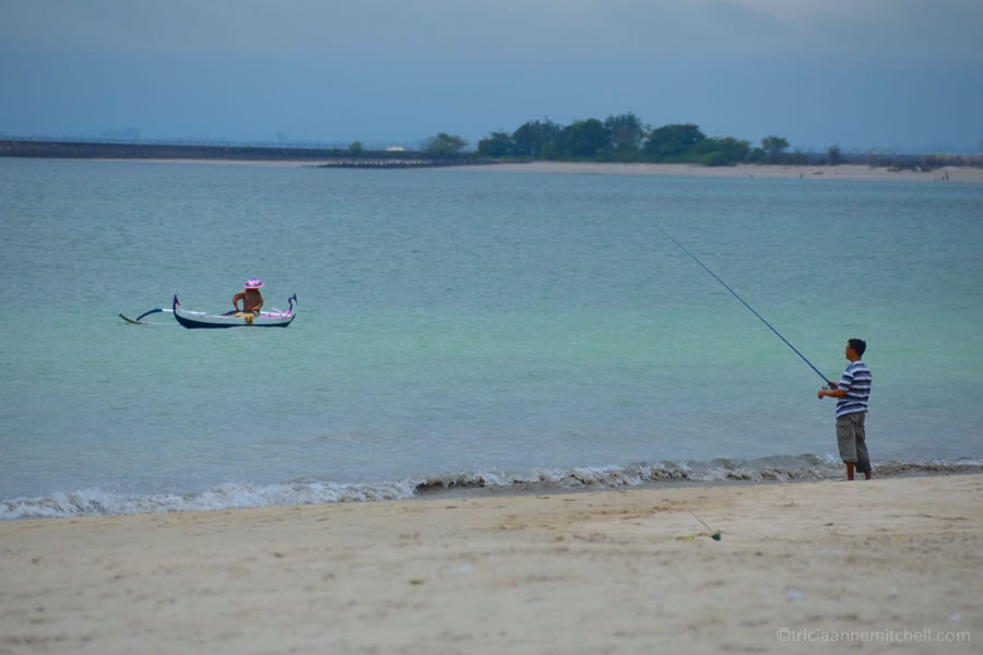 Two men fish in Jimbaran, Bali. One is in the boat, another is on the beach.