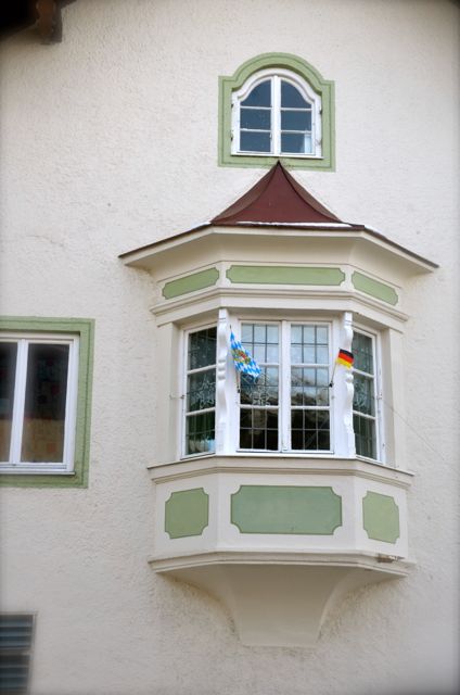 A green and white oriel window with Bavarian and German flags on an Oberammergau building.