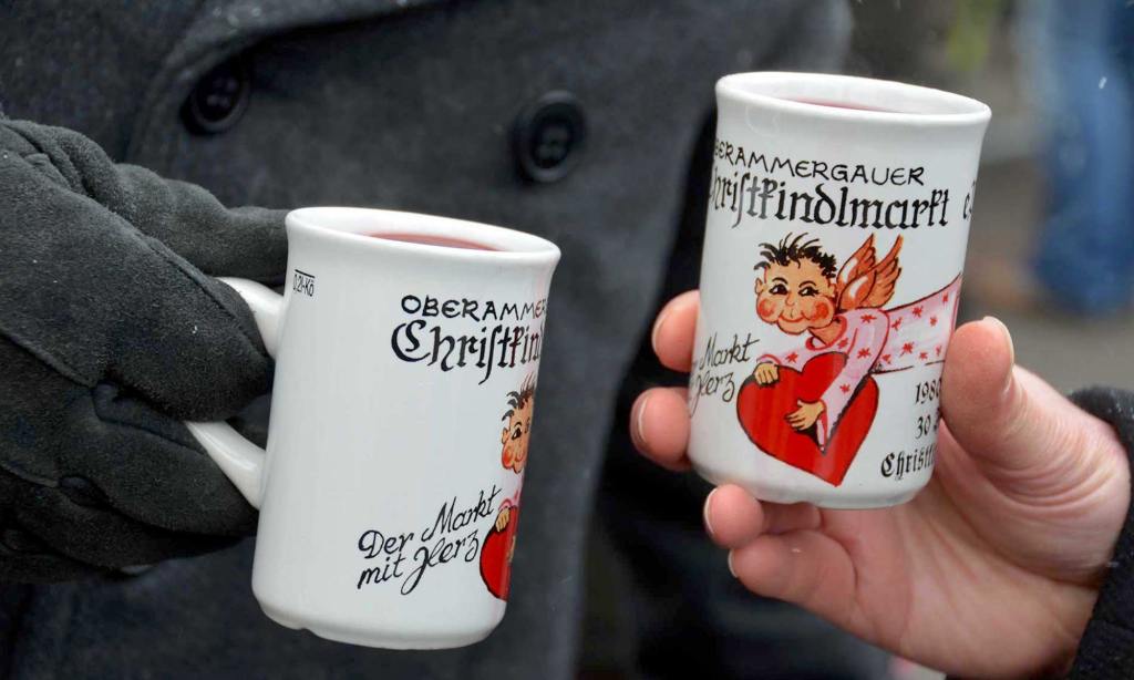 Two male hands, holding white "Christkindlmarkt" mugs filled with Gluhwein (mulled wine) at the Oberammergau, Germany Christkindlmarkt.