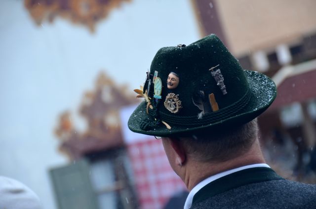 A man wears a traditional green Bavarian hat decorated with pins.
