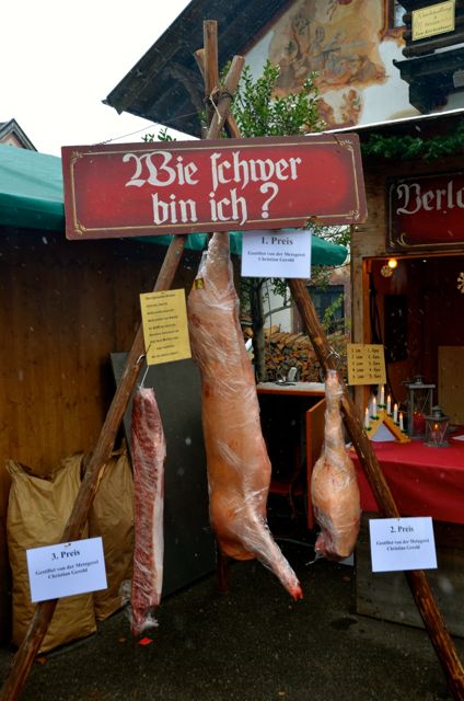 Cuts of meat hang at a German winter market with the sign "Wie schwer bin ich" or "How heavy am I?"