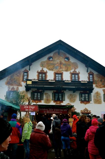 A German winter holiday market is overlooked by a traditionally painted house on a grey day.