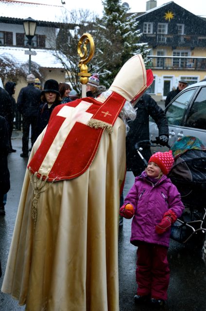 A man, dressed as St. Nicholas, hands a child an orange at a German Christkindlmarkt in Bavaria.