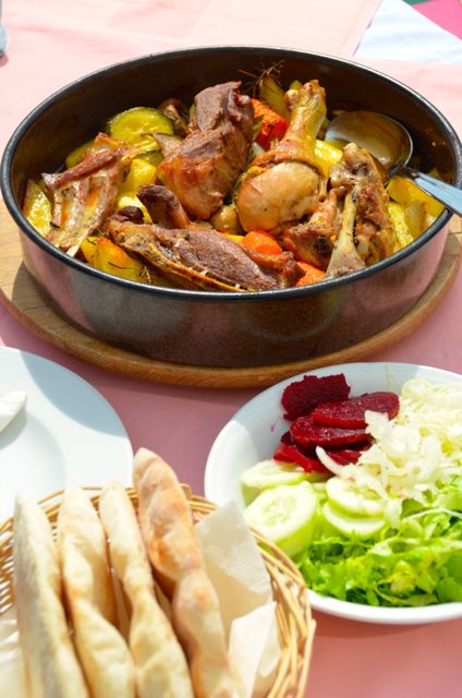 Dishes filled with peka (carrots, potatoes, and chicken), vegetables (beets, cucumbers, and lettuce) and a basket of flatbread sit on a restaurant table in Trogir, Croatia.