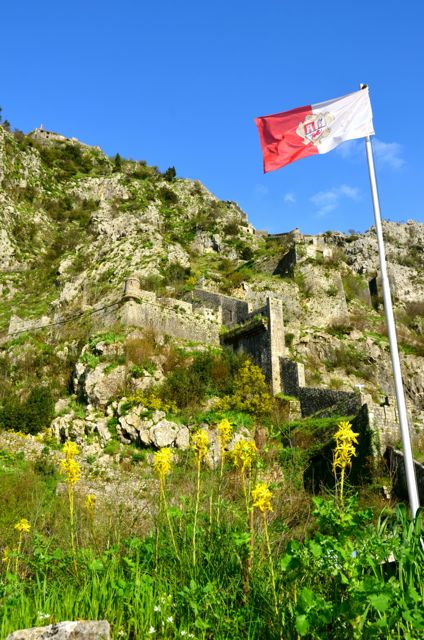 Kotor's red and white flag blows in the breeze near the town's fortress (right) and people walk into Kotor's Old Town (right)