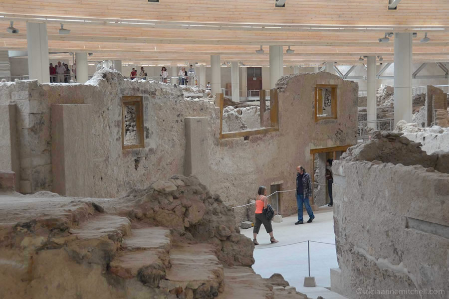 A man and woman walk through the Akrotiri archaeological site in Santorini, Greece.
