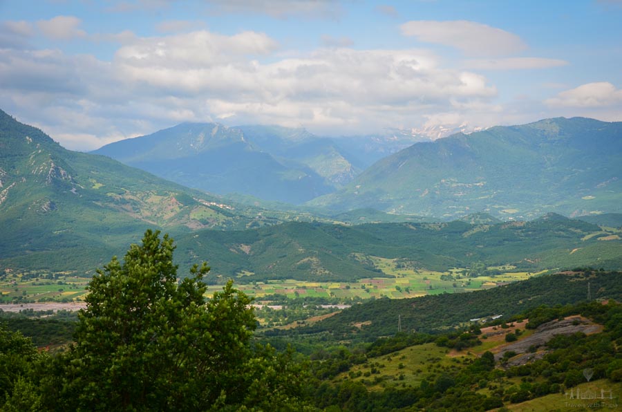 Rolling and hills carpeted with trees and greenery are visible from the monasteries of Meteora, Greece, with blue skies overhead.