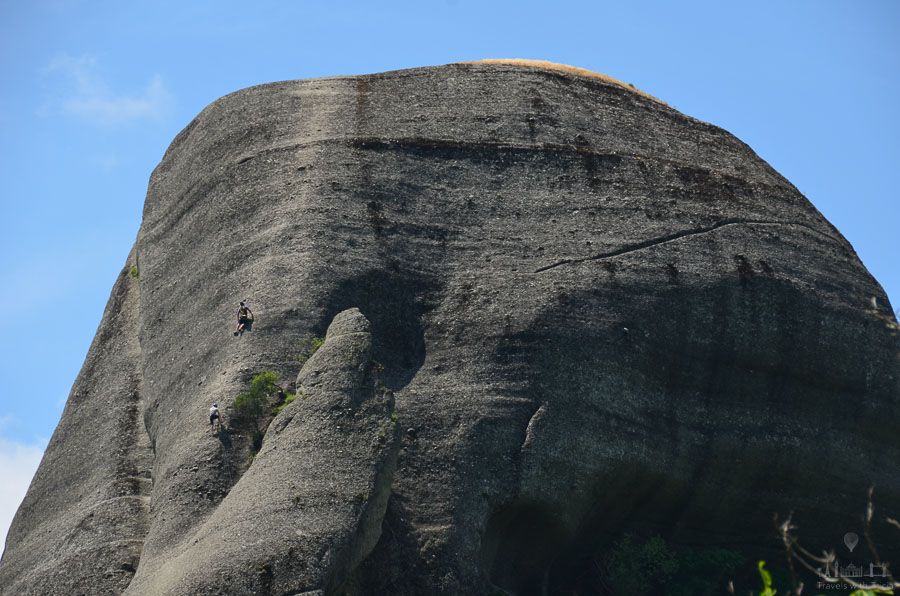 Two rock climbers scale a steep formation in Meteora, Greece.
