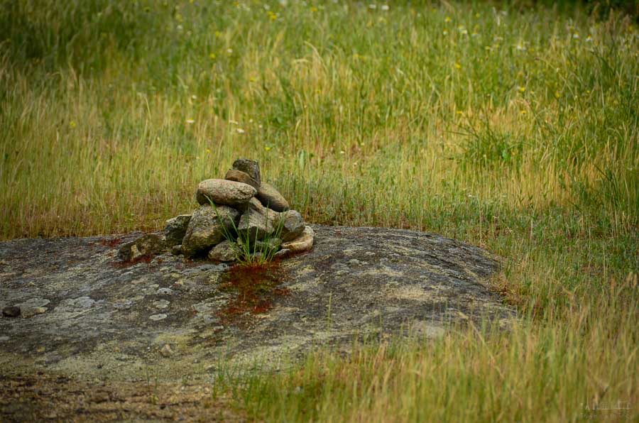 A makeshift rock towers or cairn sits among a grassy field along a hiking trail to the Meteora Monasteries in Greece.