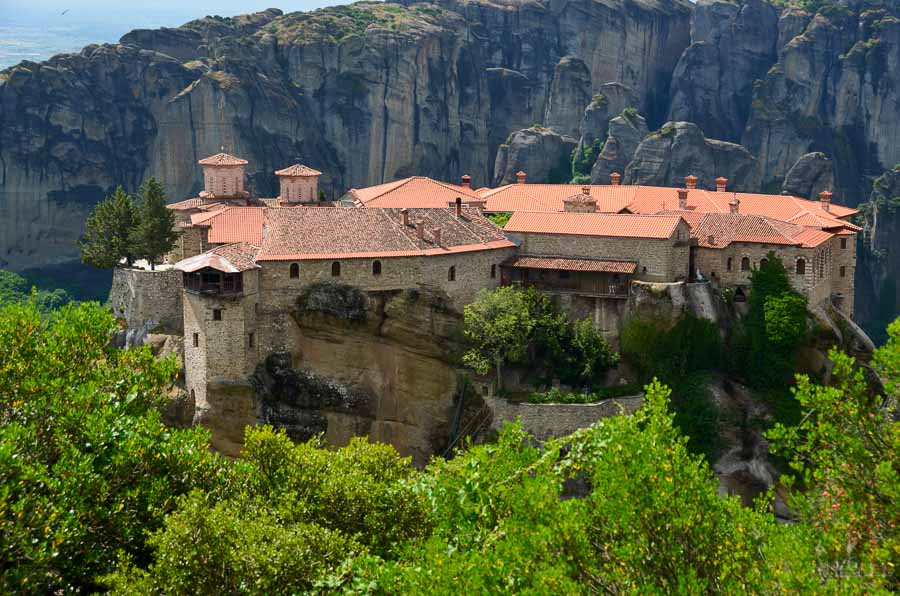 The Holy Monastery of Varlaam sits on a rocky outcrop with sandstone formations in the distance in Meteora, Greece.