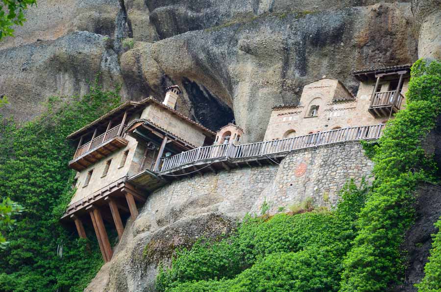 The Ypapanti Monastery clings from a sandstone rock face in Meteora, Greece, visible from a hiking trail.
