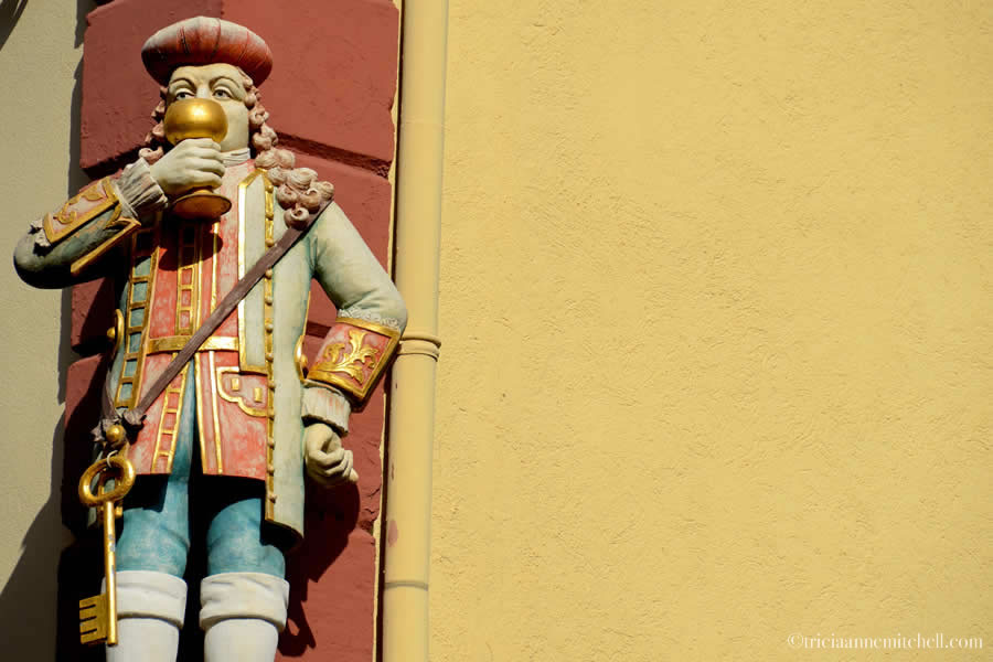 A statue of court jester Perkeo drinking wine adorns the corner of a yellow building at Haupstrasse 75 in Heidelberg, Germany.