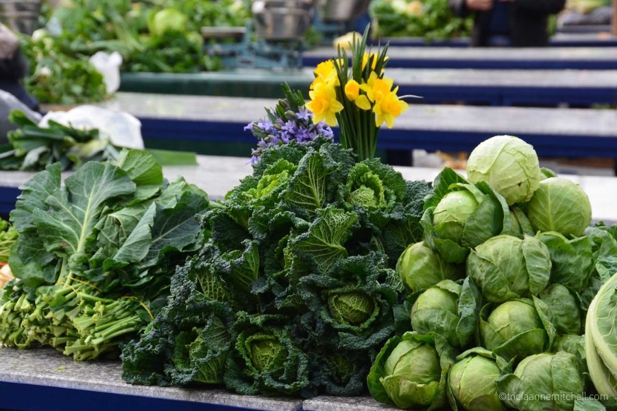 At the fresh market in Split, Croatia, spinach, kale, and cabbage sit on top of a vendor's table.