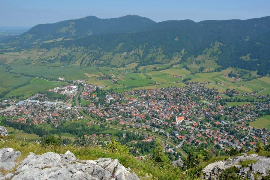 The village of Oberammergau is visible from the top of the Kofel Mountain in Germany. You can see red rooftops, the Ammer River, and green mountain slopes below.