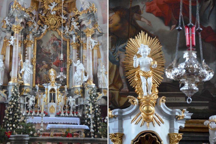 The altar of the Saint Peter and Paul Church in Oberammergau is decorated with 2 Christmas trees, silver candelabras, and poinsettia plants.