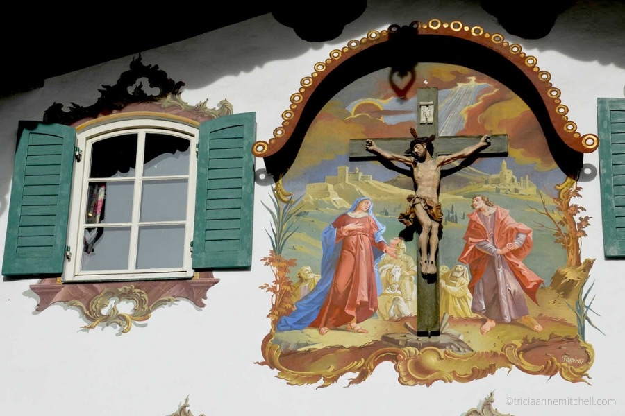 Close-up of a green-shuttered window in the German town of Oberammergau. A religious scene, complete with a crucifix, is also painted on the front of the building.