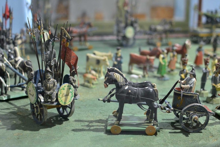 Model toy wagons and soldiers are on display on a green background inside the Oberammergau Museum.