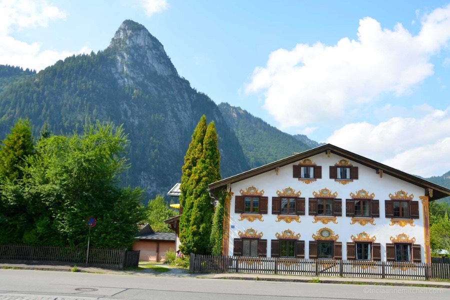A mountain peak towers over a white, chalet-style home in Oberammergau, Germany.