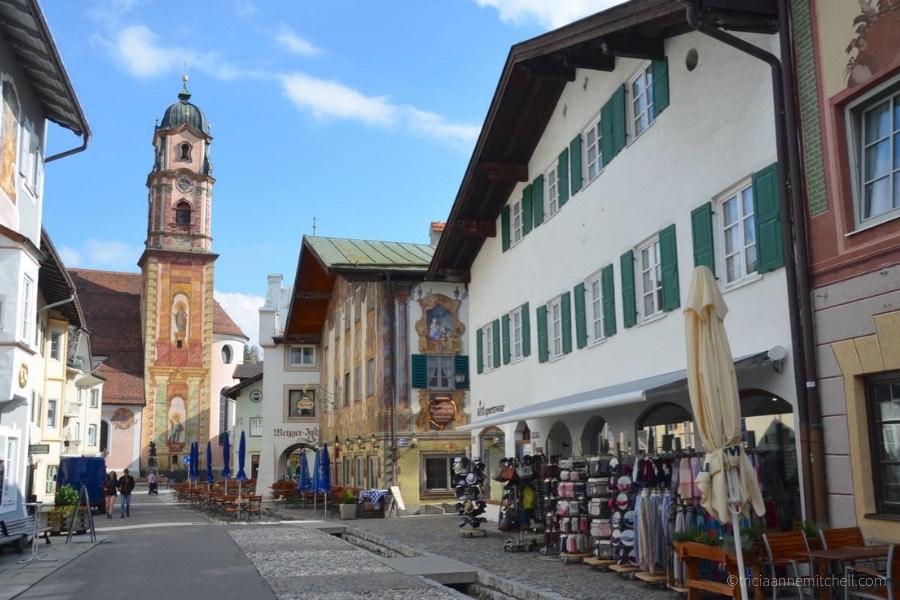 A Mittenwald, Germany street scene has painted, traditional buildings, a canal, and a church bell tower painted with frescoes.