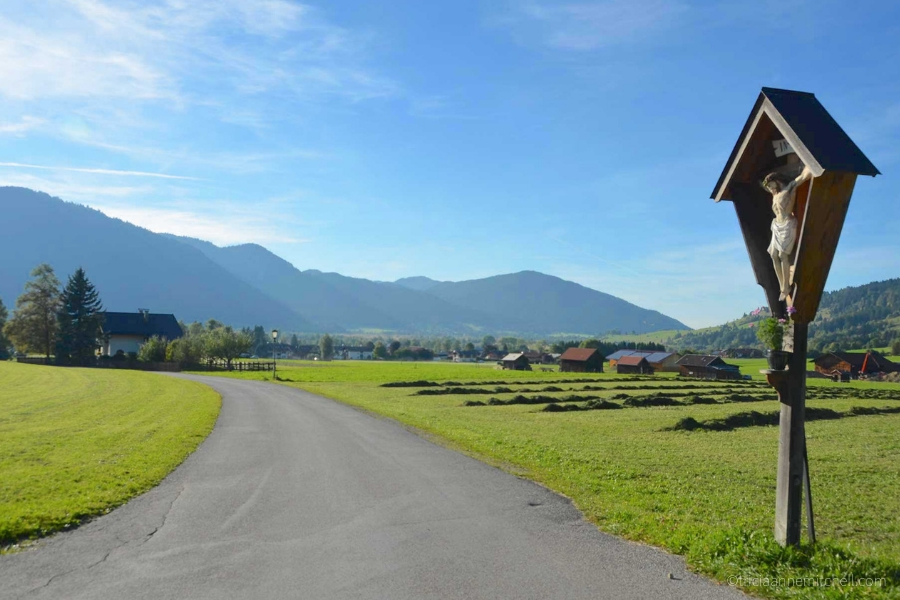 A paved road surrounding by mountains and agricultural fields in the German town of Oberammergau.
