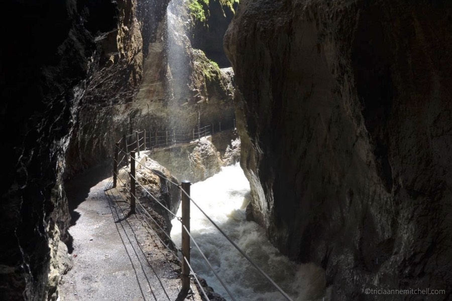 A raging river cuts through the Partnachklamm Gorge in Garmisch-Partenkirchen, Germany. Mist from a waterfall falls from overhead.