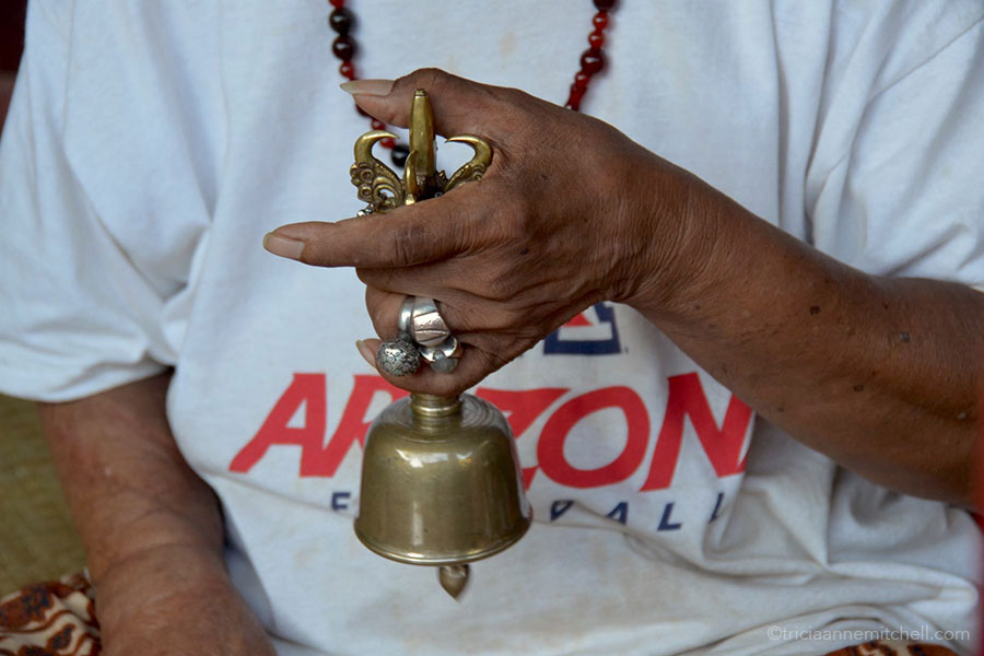 Ketut Liyer Sounding Bell A man's hand is visible, ringing a brass bell.