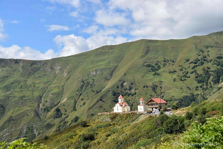 Two churches and a chalet-style house rest on a plateau among mountainous landscape near Gudauri Ski Resort in the Republic of Georgia.