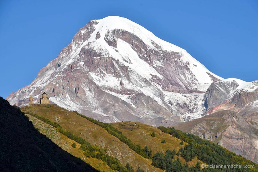 A snowy Mt. Kazbek towers over the beige-colored towers of the Gergeti Trinity Church in Georgia.