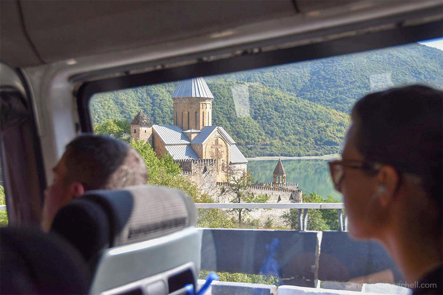 A brick church / fortress is visible through the window of a minivan in the Republic of Georgia. Two passengers also gaze out the window.
