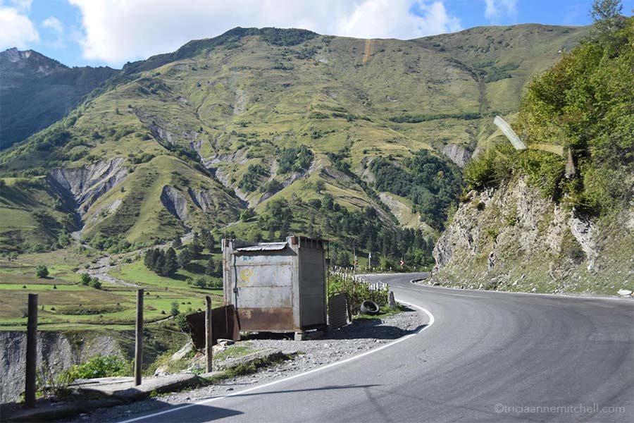 A road curves around green mountain slopes in the Republic of Georgia. It is the Georgian Military Highway.