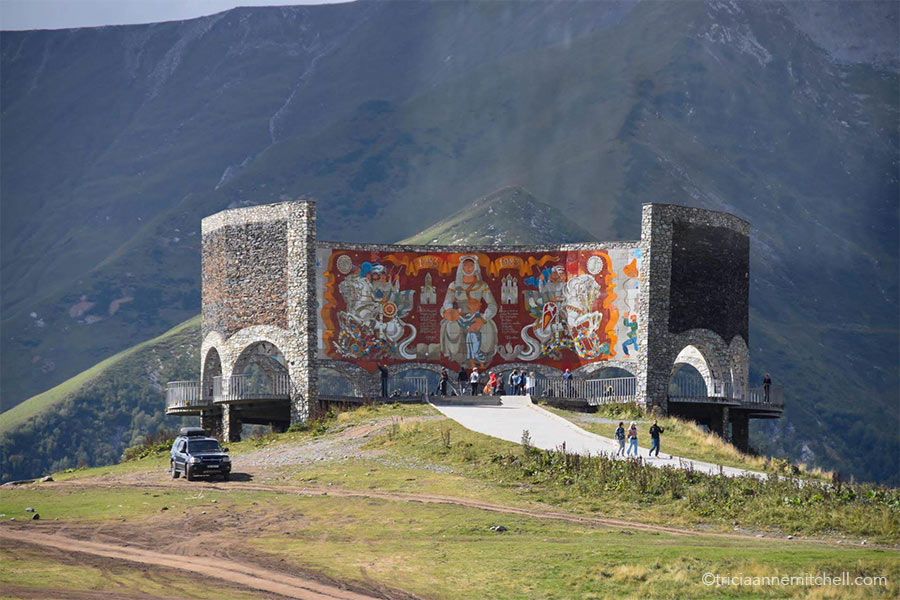 A front view of the Russia–Georgia Friendship Monument painted interior. It includes a red background and historic figures, some of whom are on horseback.